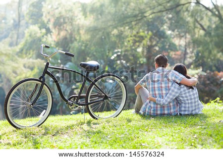 back view of romantic teenage couple sitting outdoors with bicycle next to them