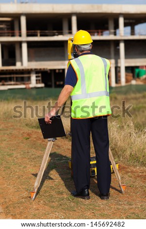 rear view of senior land surveyor working at construction site with theodolite