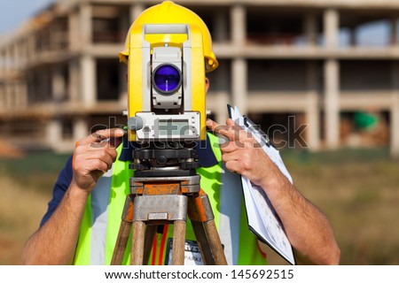 land surveyor looking through theodolite at construction site