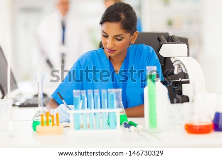 beautiful young indian medical researcher writing report in lab