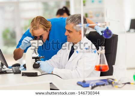 two male medical researchers working with microscope in lab