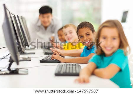 smiling group children in computer class with teacher on background