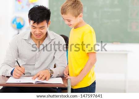 cheerful young male teacher grading school boy\'s work