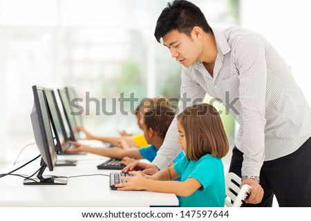 young elementary school teacher teaching students in computer room