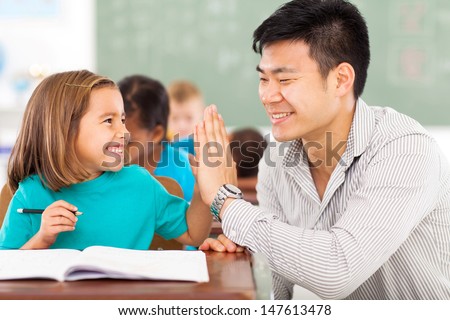 Cheerful Elementary School Teacher And Student High Five In Classroom