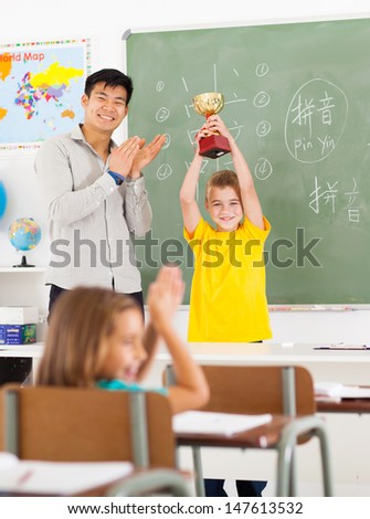 cheerful male chinese language teacher applauding for student who won a trophy