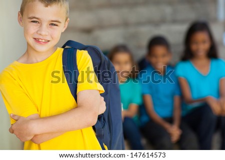 cute young primary schoolboy with arms crossed in front of classmates