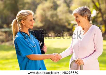 beautiful mid aged nurse handshaking senior patient outdoors