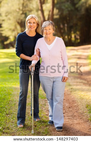 smiling senior woman and caring daughter walking in forest