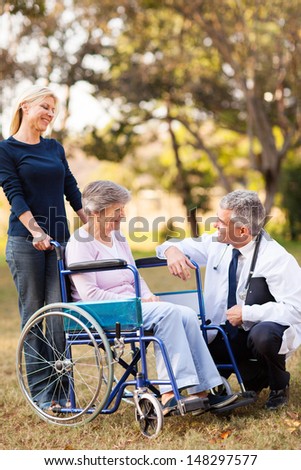 smiling middle aged healthcare worker talking to senior handicapped patient and daughter outdoors