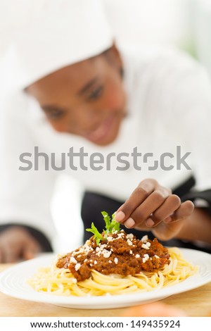 female african cook garnishing spaghetti in modern kitchen