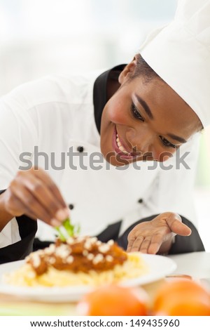 happy african american chef in kitchen decorating pasta dish
