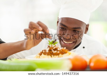 portrait of Afro American chef in restaurant kitchen garnishing pasta dish