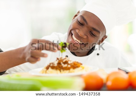 cheerful african chef decorating spaghetti