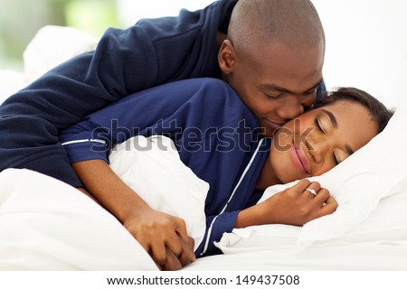 smiling african man in bed kissing wife in bed