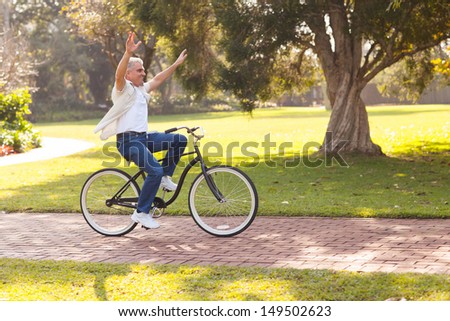 playful middle aged man riding a bike outdoors with arms up