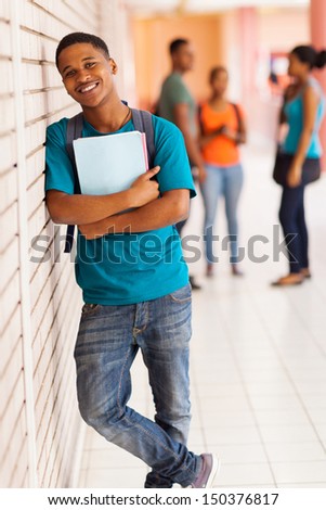 handsome african college boy standing with books against the wall