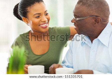 smiling elderly african american man enjoying coffee with his granddaughter at home