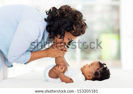 happy african american mother kissing baby feet while playing on bed happy african american mother kissing baby feet while playing on bed