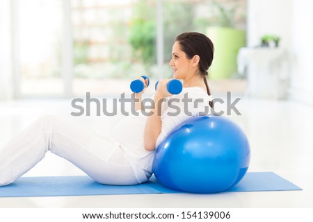 pretty pregnant woman exercising with dumbbells at home