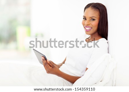 pretty african woman holding tablet computer on bed