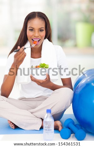 pretty afro american woman eating salad on exercise mat