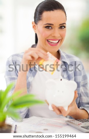 cheerful young woman putting money in piggy bank