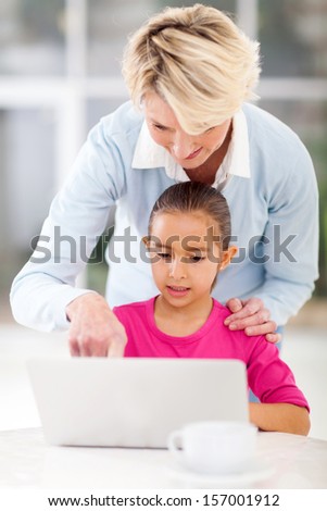 senior grandmother teaching grandchild how to use laptop computer at home