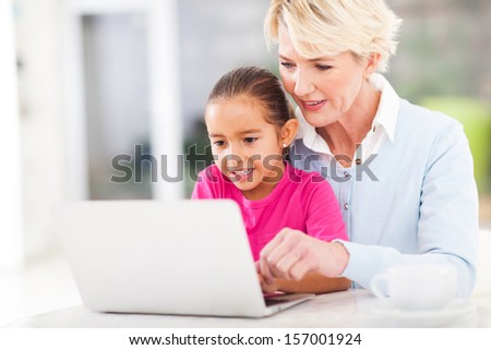modern grandmother teaching grandchild how to use laptop computer at home