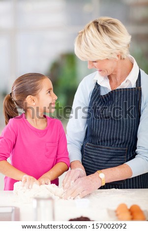 adorable little girl helping her grandmother baking in kitchen
