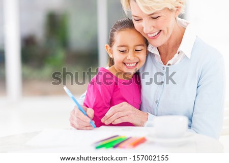 happy senior grandmother teaching her granddaughter how to draw at home