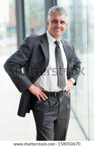 happy senior businessman portrait in office with hands on waist