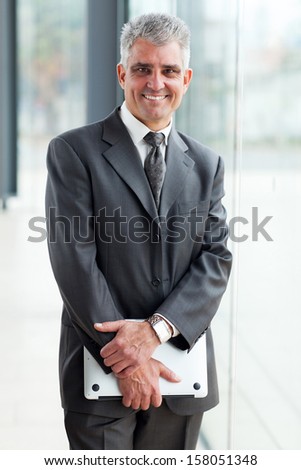 happy middle aged businessman holding laptop in office
