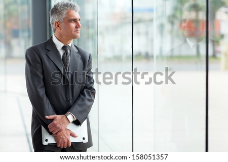 thoughtful mid age businessman looking through office window