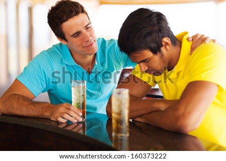 young man sitting at bar and comforting his sad friend