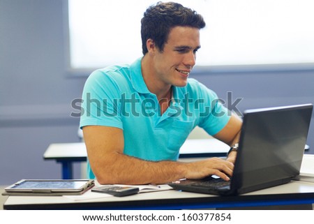 cute male university student using laptop in lecture room