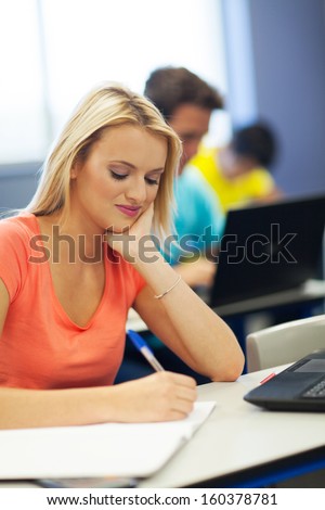pretty female university student writing class work in classroom