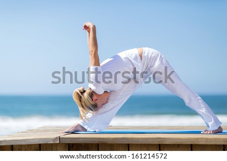 flexible mid age woman doing yoga pose on beach