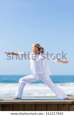 senior woman doing warrior yoga pose at the beach