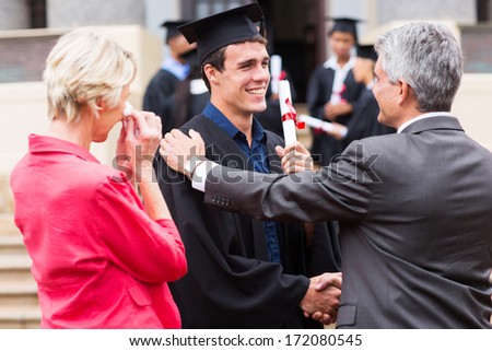 handsome male graduate being congratulated by his father at graduation ceremony