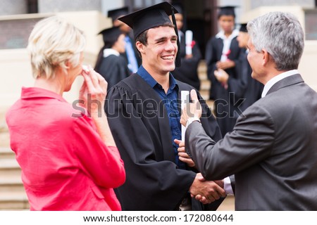 cheerful male graduate handshaking with his grandfather