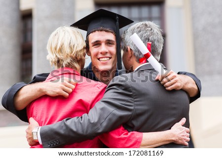 handsome young male graduate hugging his parents at graduation