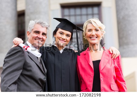 beautiful young female graduate with parents at ceremony
