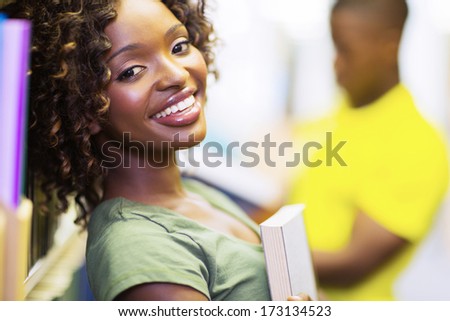 pretty female african uni student holding a book in library