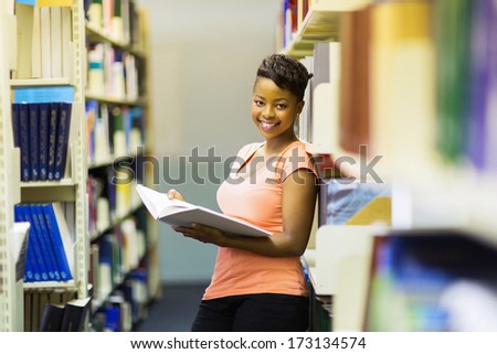 female african american college student leaning on book shelf in library