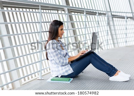 female university student sitting on the floor working on laptop computer