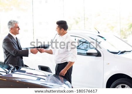 senior car salesman handing over new car key to customer at showroom