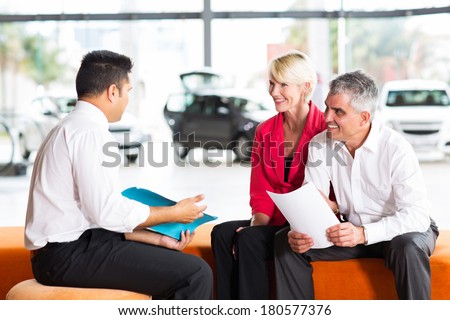 vehicle salesman explaining contract to senior couple before buying a car