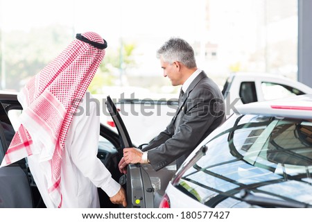 Arabian man getting in a new car for test drive at vehicle dealership