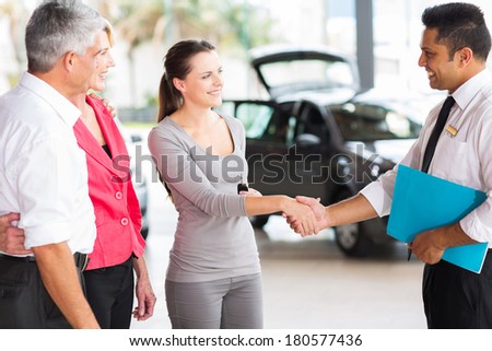 vehicle salesman handshaking with young adult customer after the sale